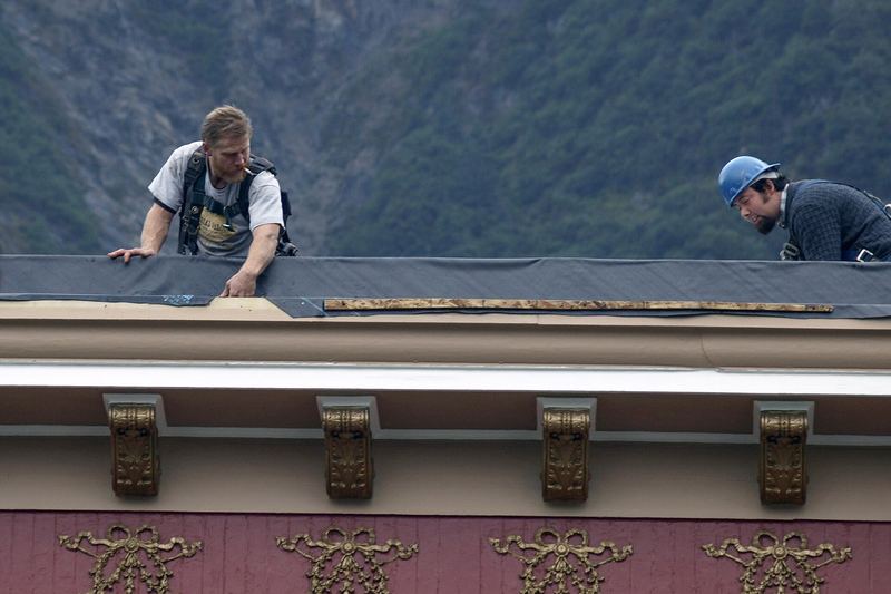 Roofers refurbishing a roof above a decorative cornice